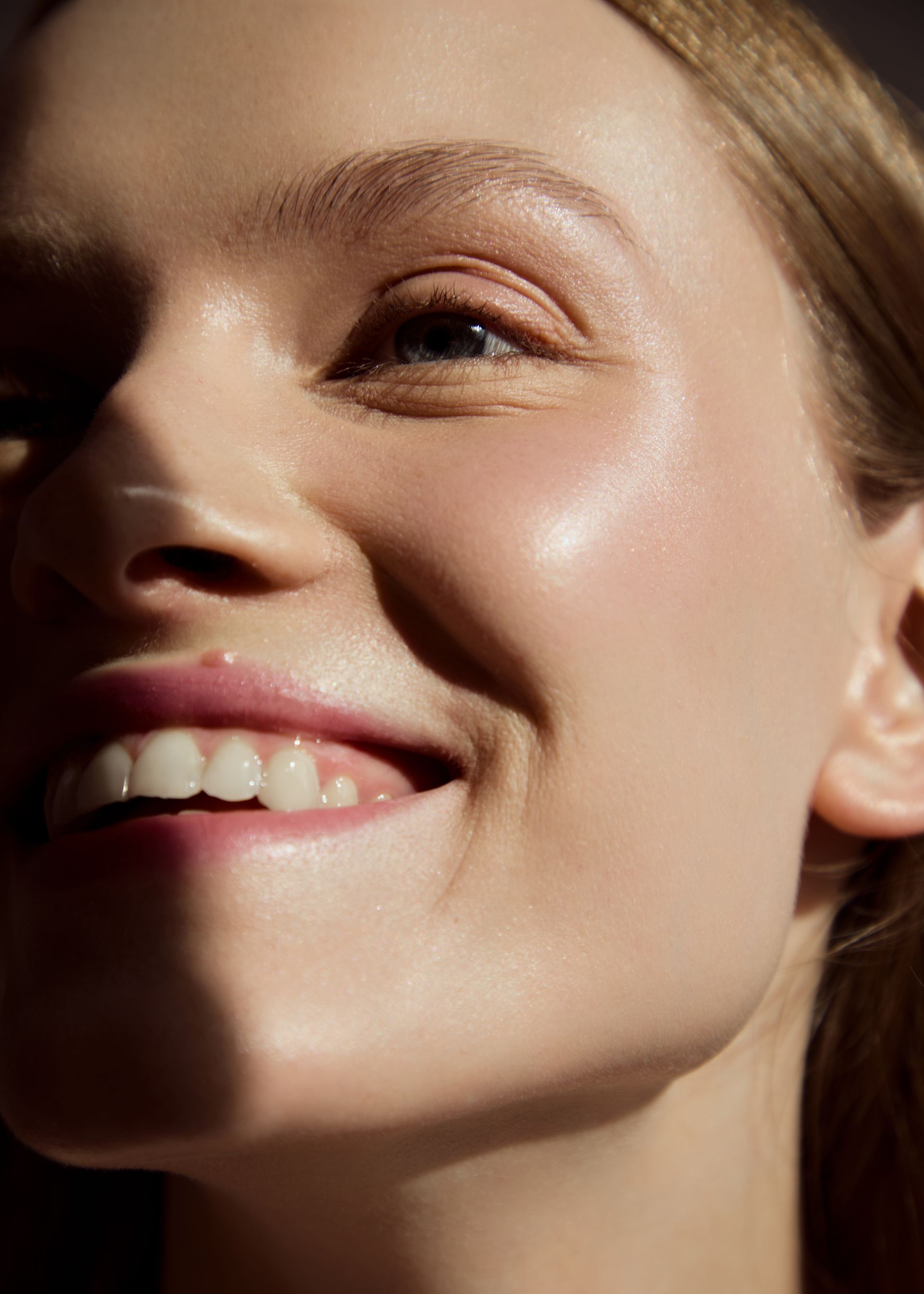 Smiling woman with blonde hair, lit by sunlight, showcasing glowing skin.