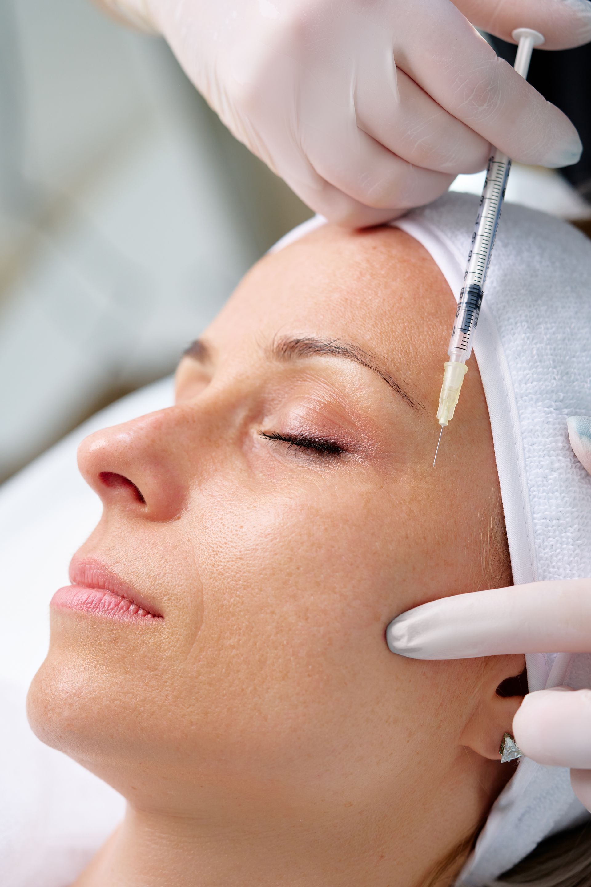 Person receiving a facial injection; gloved hands with syringe near eye.