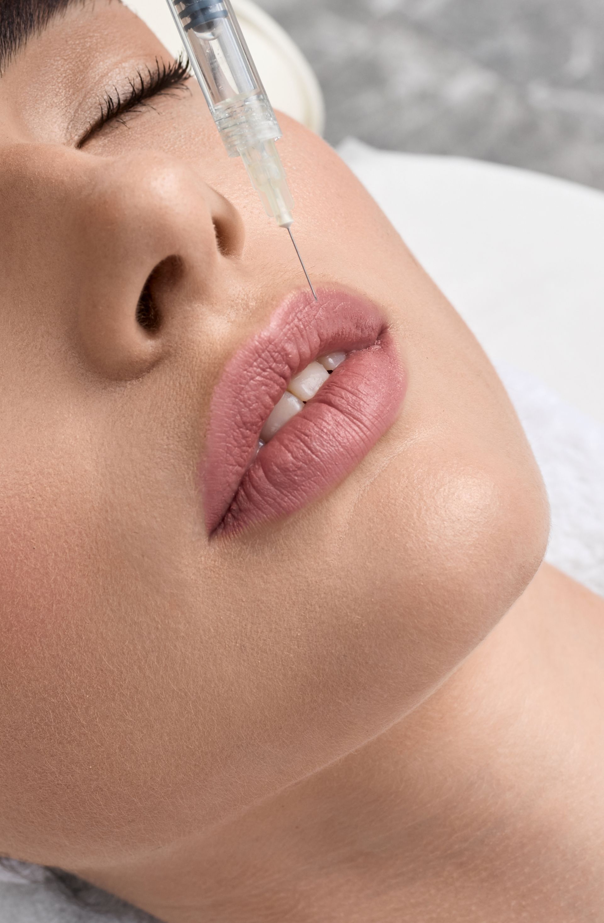 A person receiving lip filler injections. Syringe near lip. Eyes are closed.