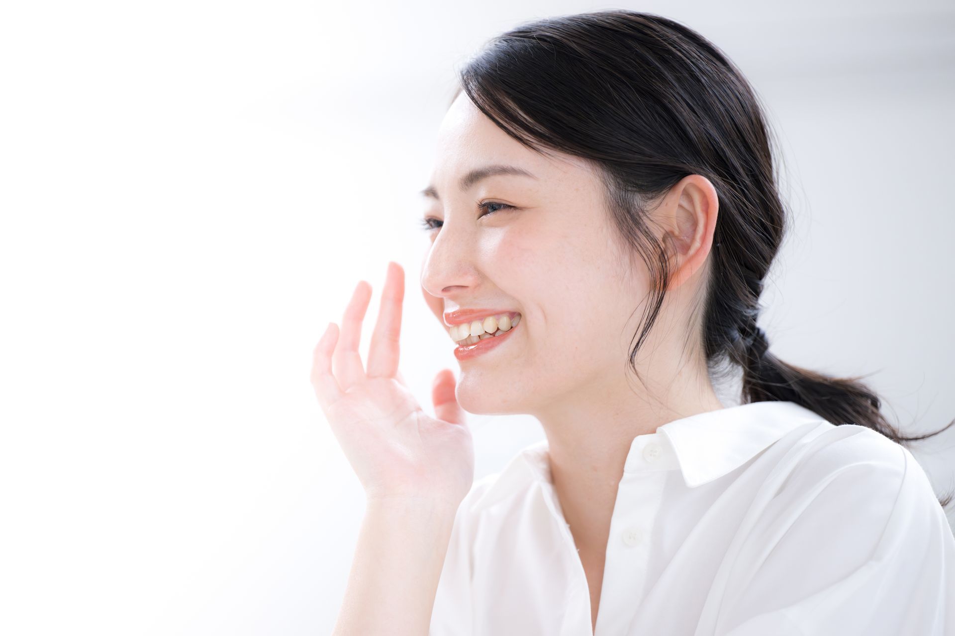 Woman smiling, hand near face, light background.