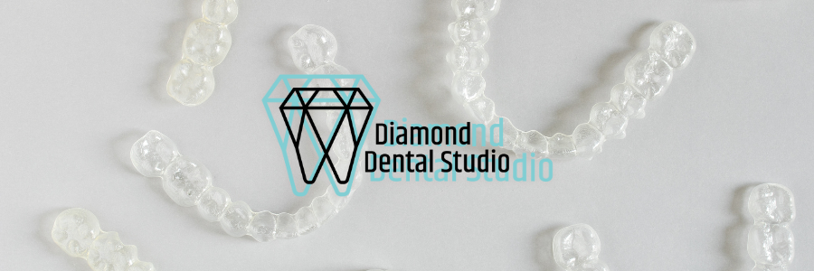 Clear aligners arranged on a white surface with Diamond Dental Studio logo.
