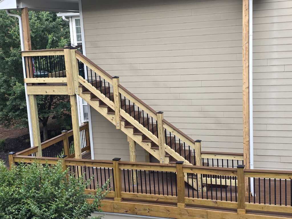 Wooden deck and stairs leading up to a house. Black railing, beige siding.