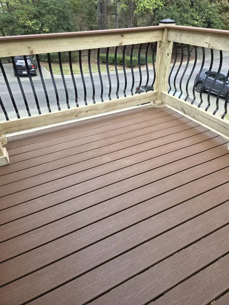 Deck with brown composite decking, black railing, and wooden handrails, with cars visible in the background.