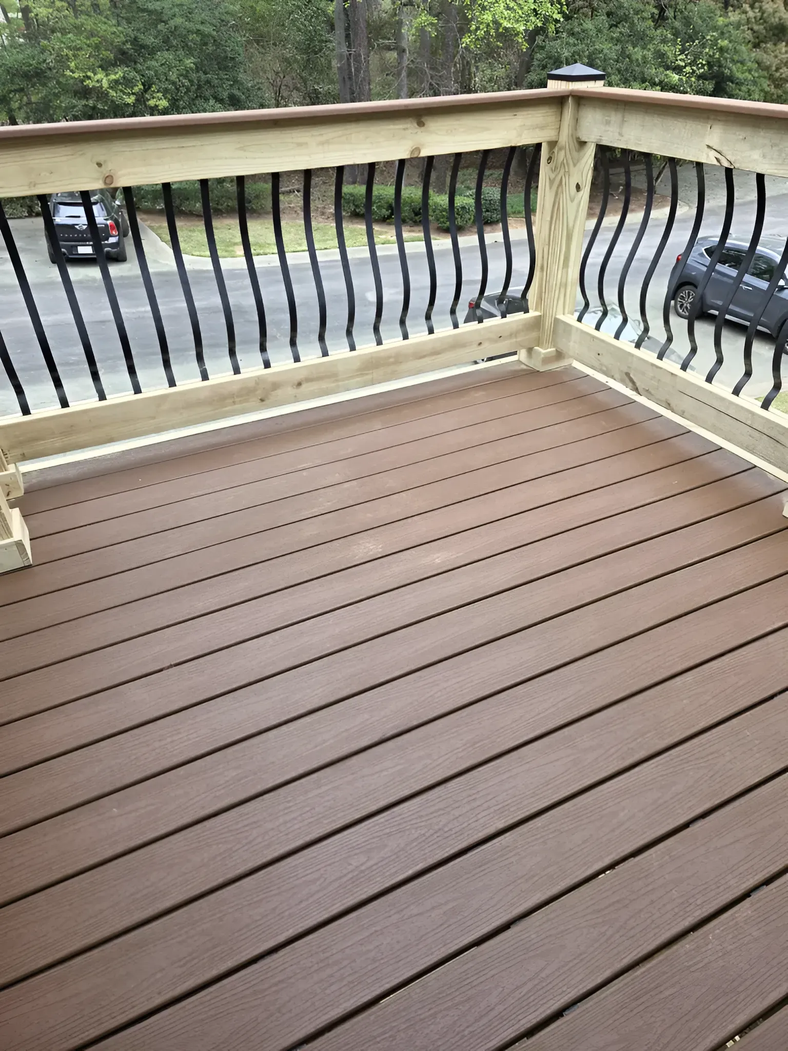 Brown composite deck with black metal railing, overlooking a street with cars.
