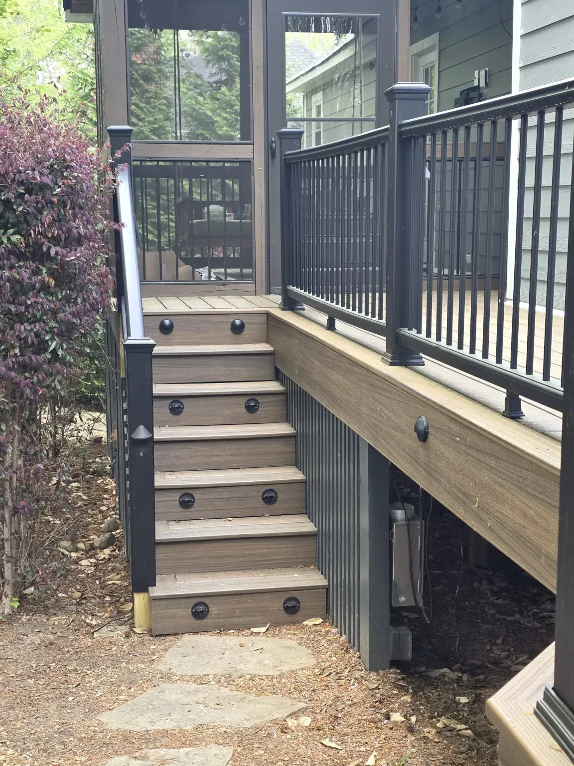 Wooden deck with stairs, black railing, and screened-in porch entrance.