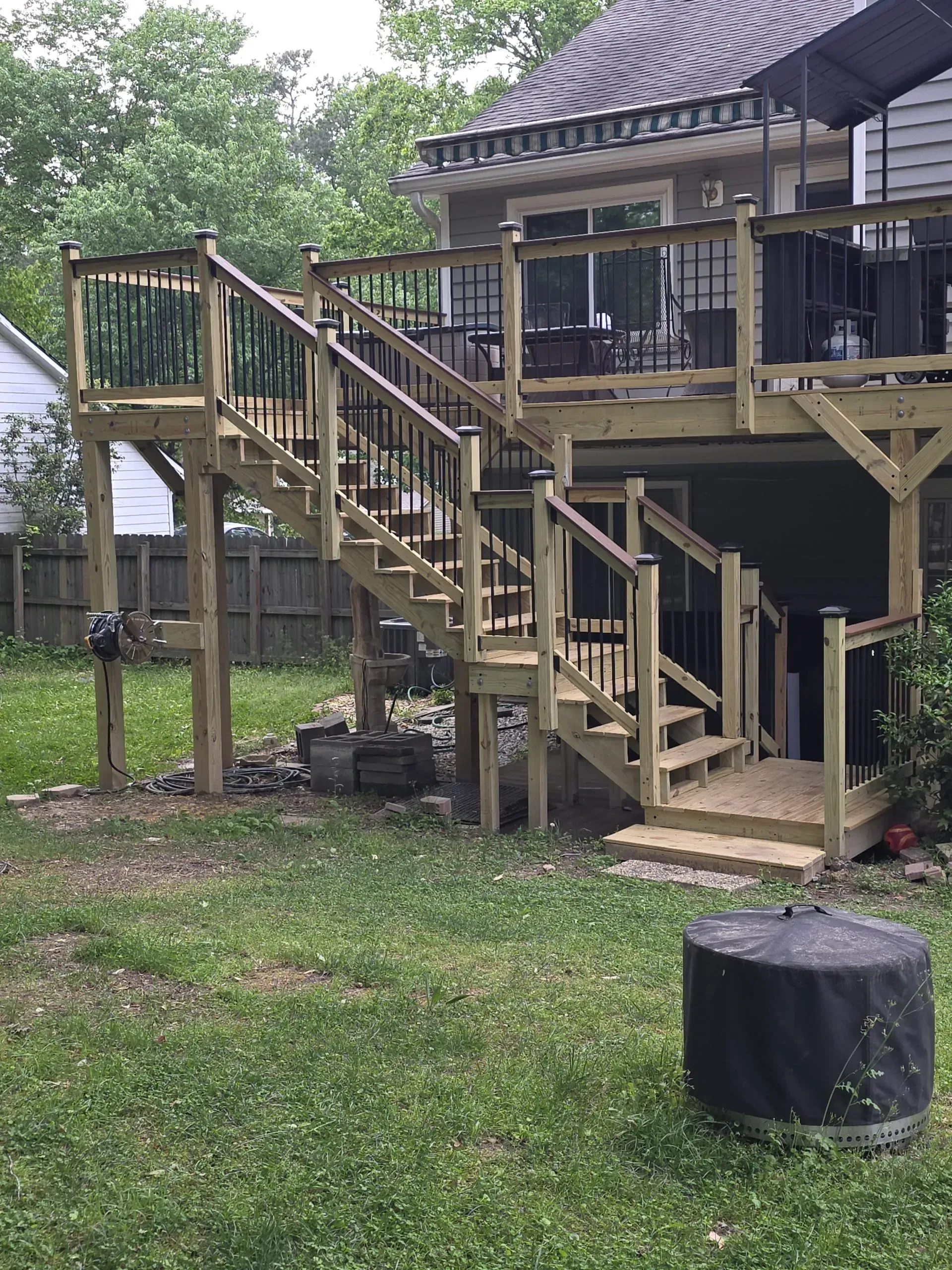 Wooden deck with stairs leading to backyard. Black railings and supports. Gray roof visible. Green grass.