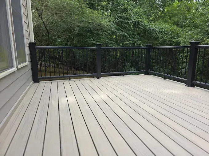 Gray composite deck with black railing and lush green trees in the background.