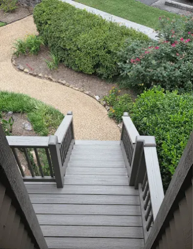 Wooden stairs leading down to a gravel path bordered by bushes and landscaping.