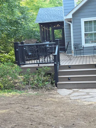 Deck and steps leading to a screened porch, with a gray house in the background.
