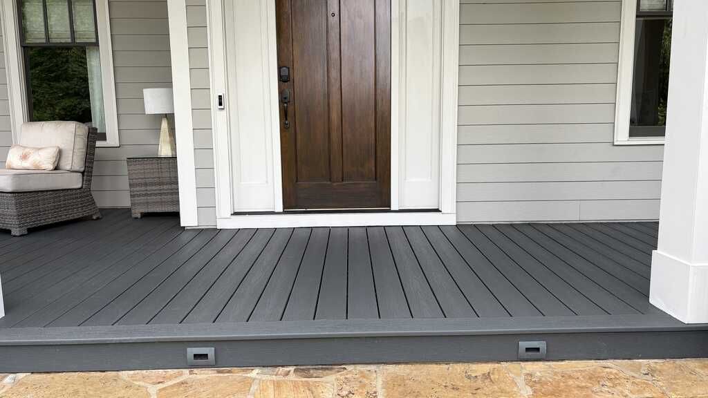 Gray wooden porch with brown door, seating, and step lights.