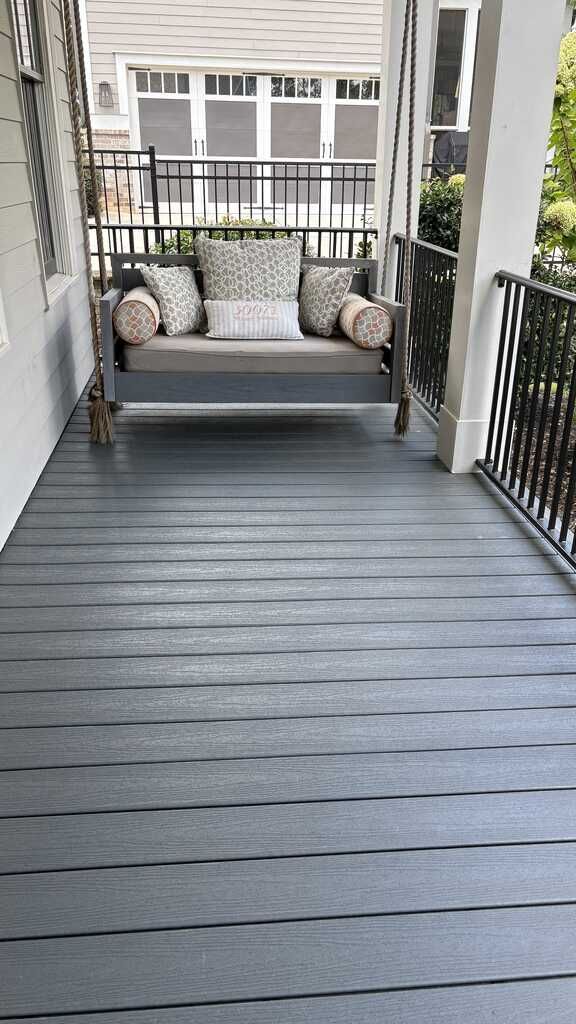Porch with gray composite decking and a wooden swing. Black wrought iron railing.