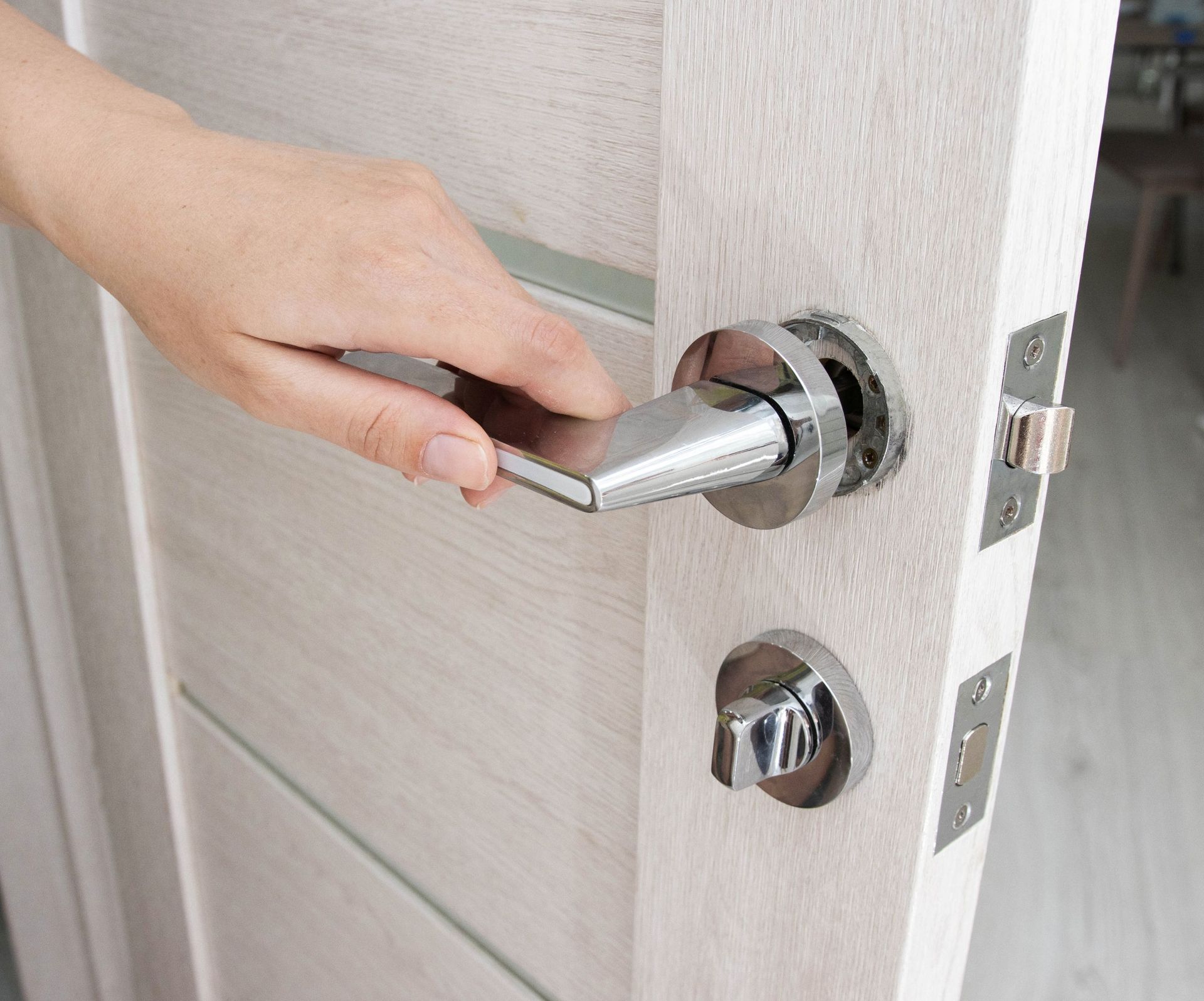 Hand opening a silver door handle on a white door.