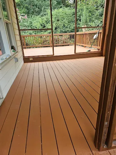Brown painted deck with screened porch, overlooking a green wooded area.