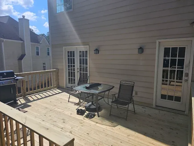 Wooden deck with a table, chairs, and grill next to a beige house with French doors.