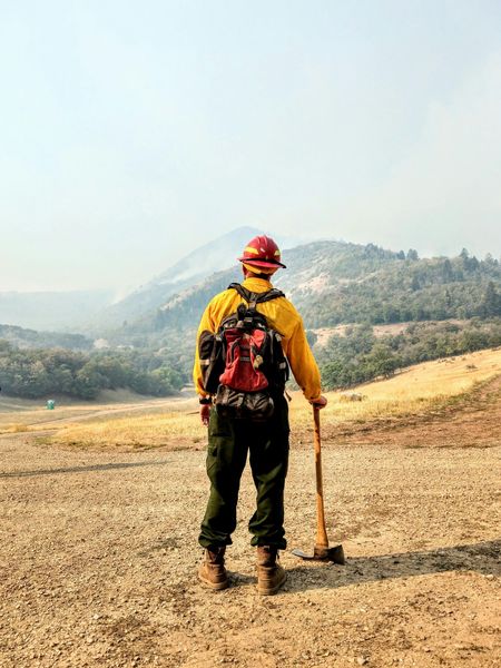 A firefighter is standing in the middle of a field holding a shovel.