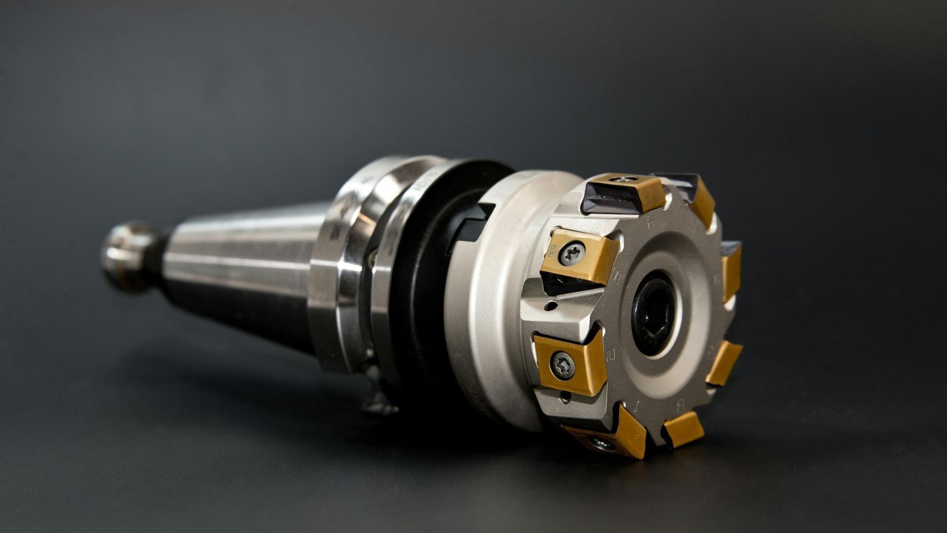 Metal milling cutter tool with gold and silver blades on a dark background.