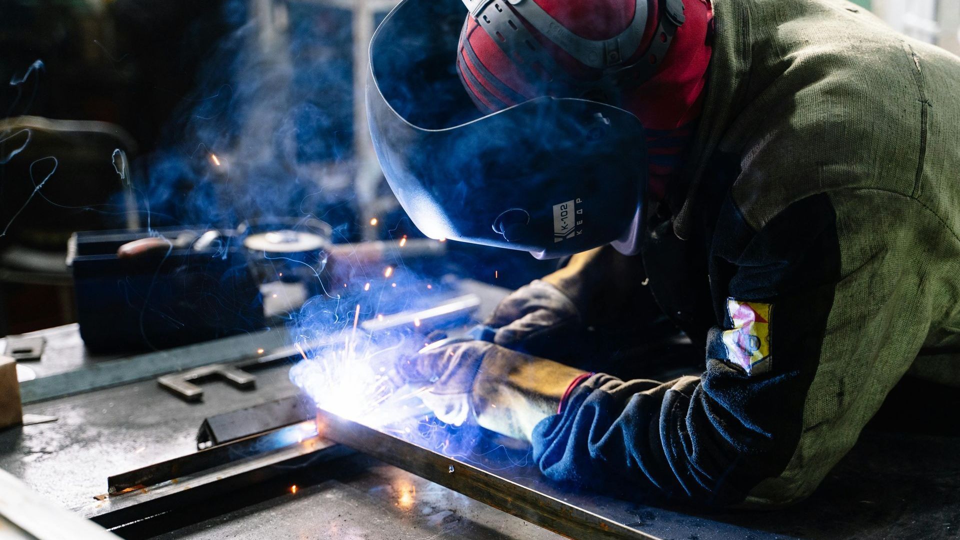 Welder in protective gear, welding metal with bright sparks in a workshop.