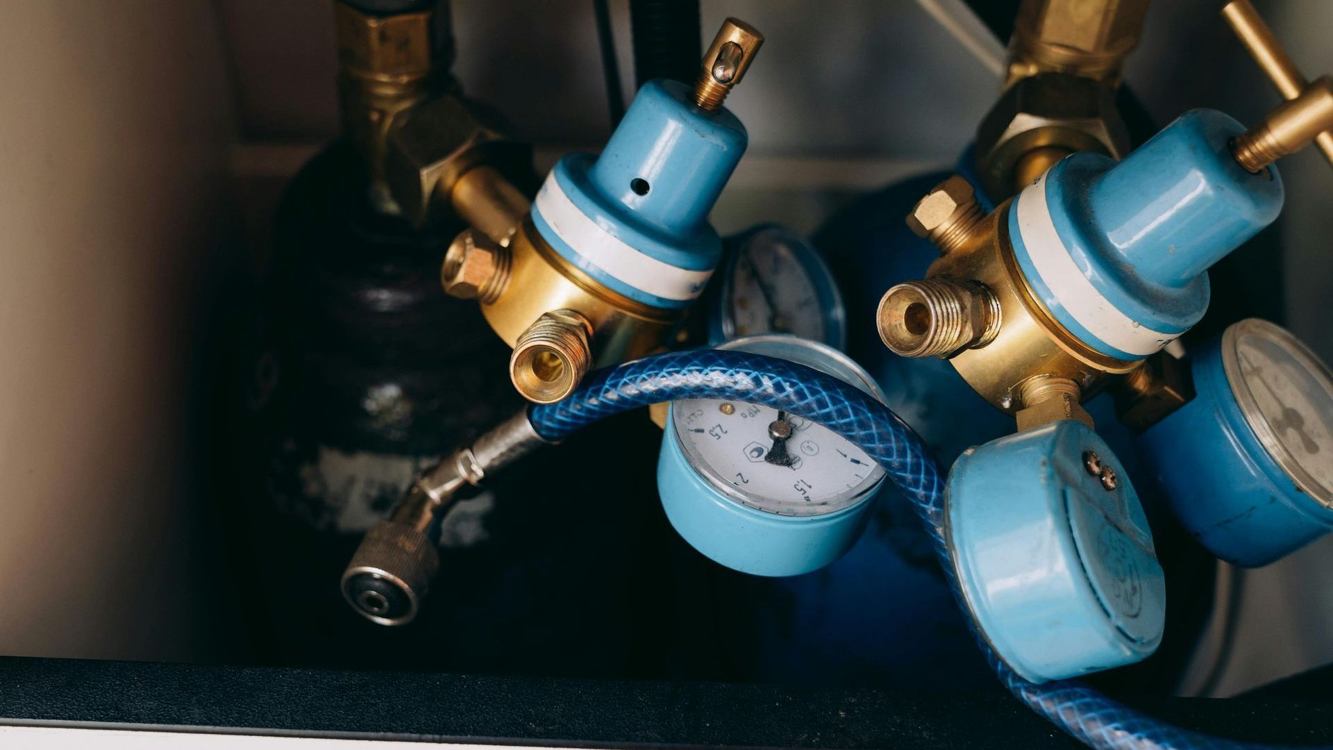 Blue and gold gas regulators with gauges and a connecting hose.