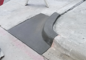New concrete ramp at a curb, gray and curved, blending into sidewalk and street.