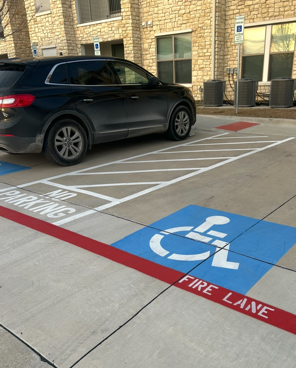 Black SUV parked in handicapped space, next to fire lane with blue and red markings, outside building.