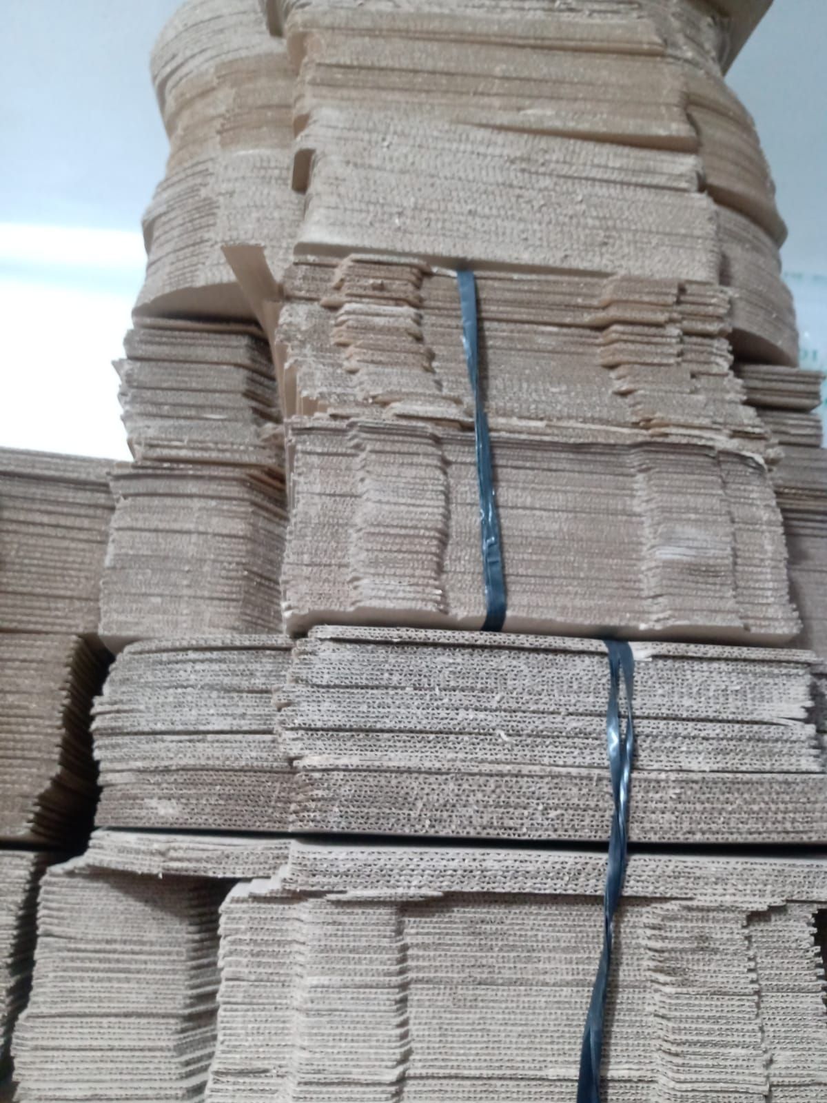 Una pila alta y vertical de cajas de cartón marrón planas y plegadas, unidas entre sí por flejes de plástico negro.