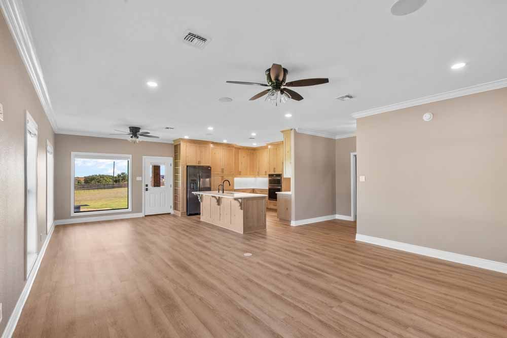 Open-concept living space with kitchen. Beige walls, wood-look flooring, light wood cabinets, and two ceiling fans.