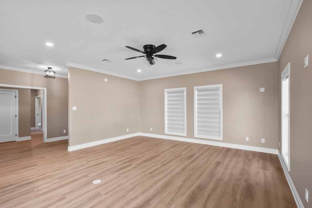 Empty room with wood floors, tan walls, white trim, recessed lighting, and a ceiling fan.