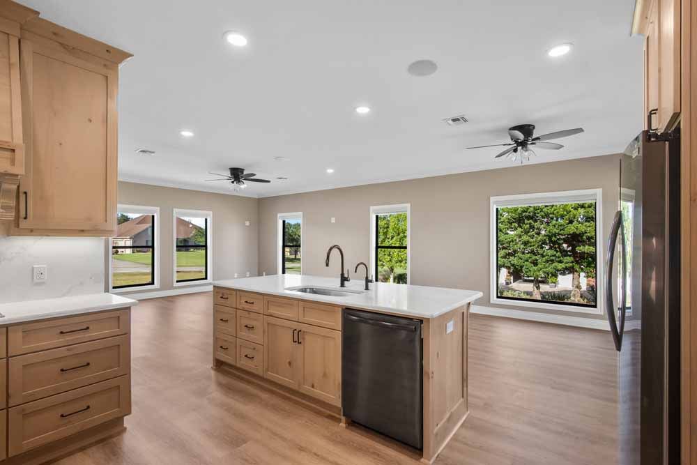 Open-plan kitchen with wood cabinets, island with sink, and large windows.