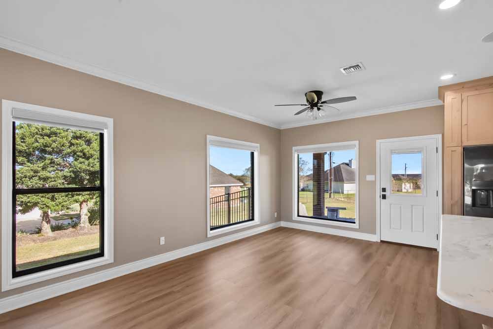 Empty room with windows, door, and ceiling fan; neutral walls, wood-look floor, and water views.