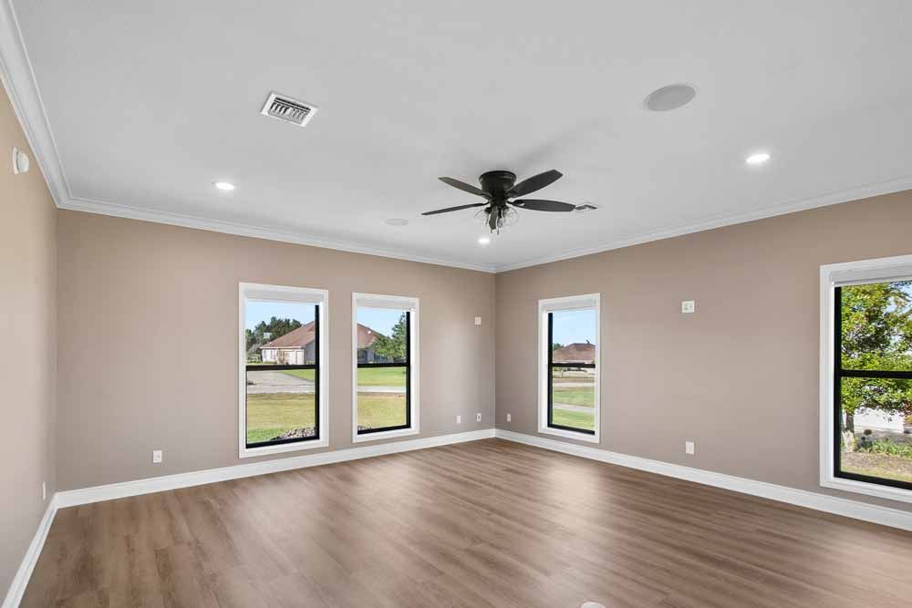 Empty room with wood floors, tan walls, large windows, and a ceiling fan.