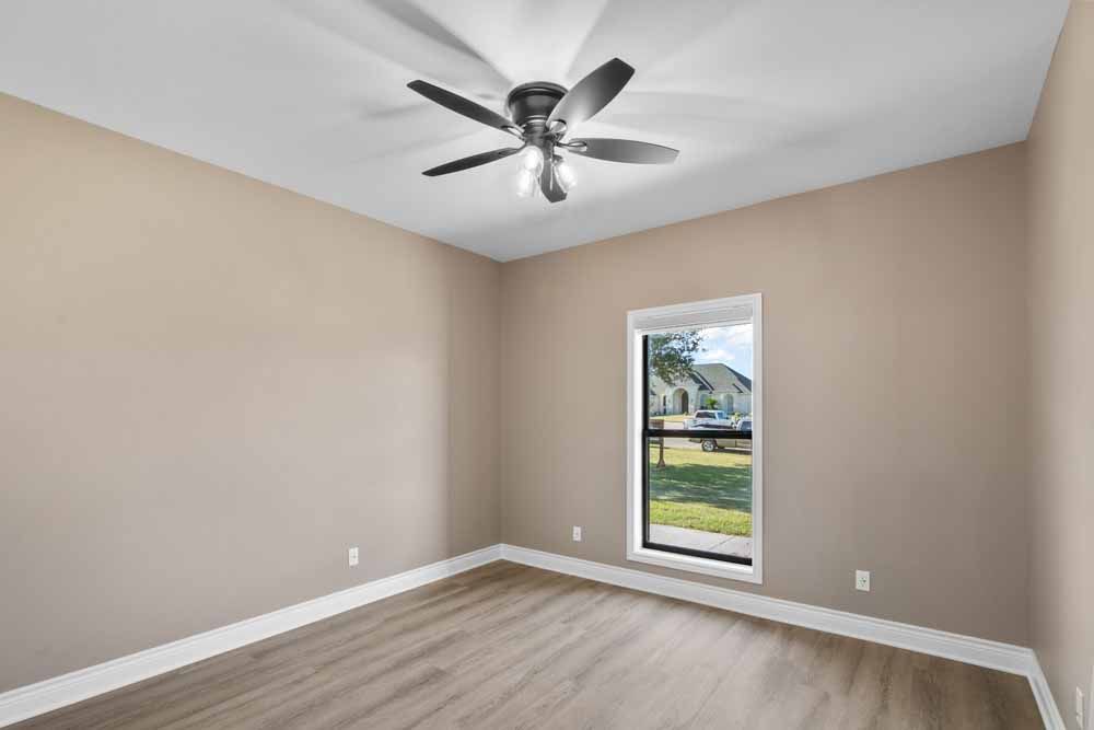 Empty room with beige walls, ceiling fan, window, and wood-look flooring.