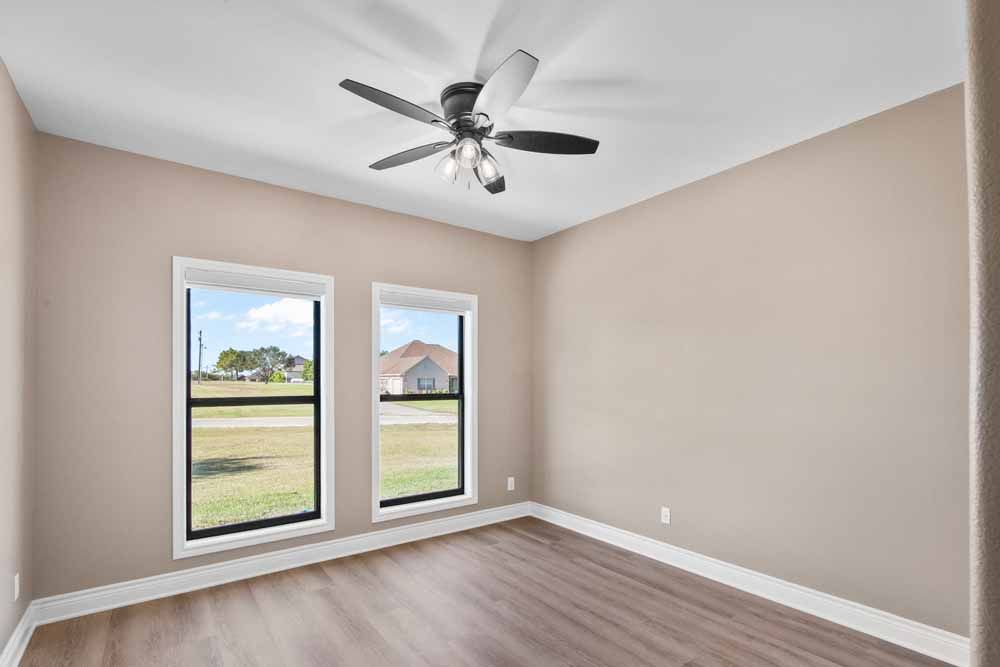 Empty room with beige walls, two windows, ceiling fan, and wood-look flooring.