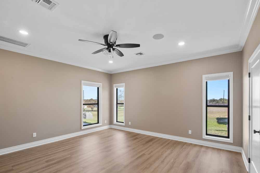 Empty room with three windows, a ceiling fan, and recessed lights. Beige walls, wood floor, white trim.