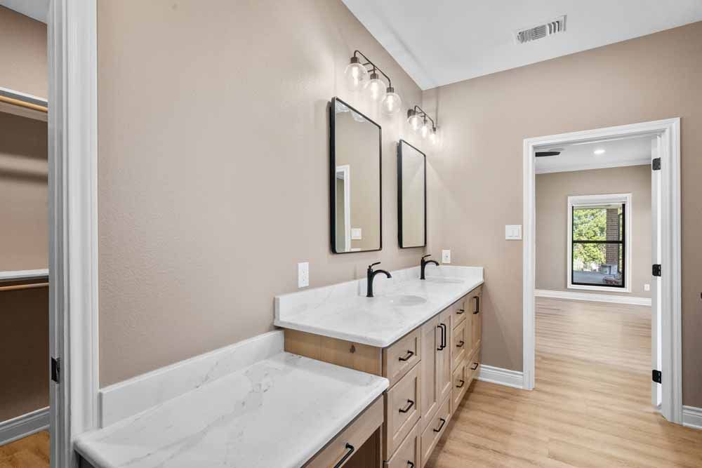 Bathroom with double vanity, two mirrors, and a walk-in closet. Beige walls, wood cabinets, and light wood floors.