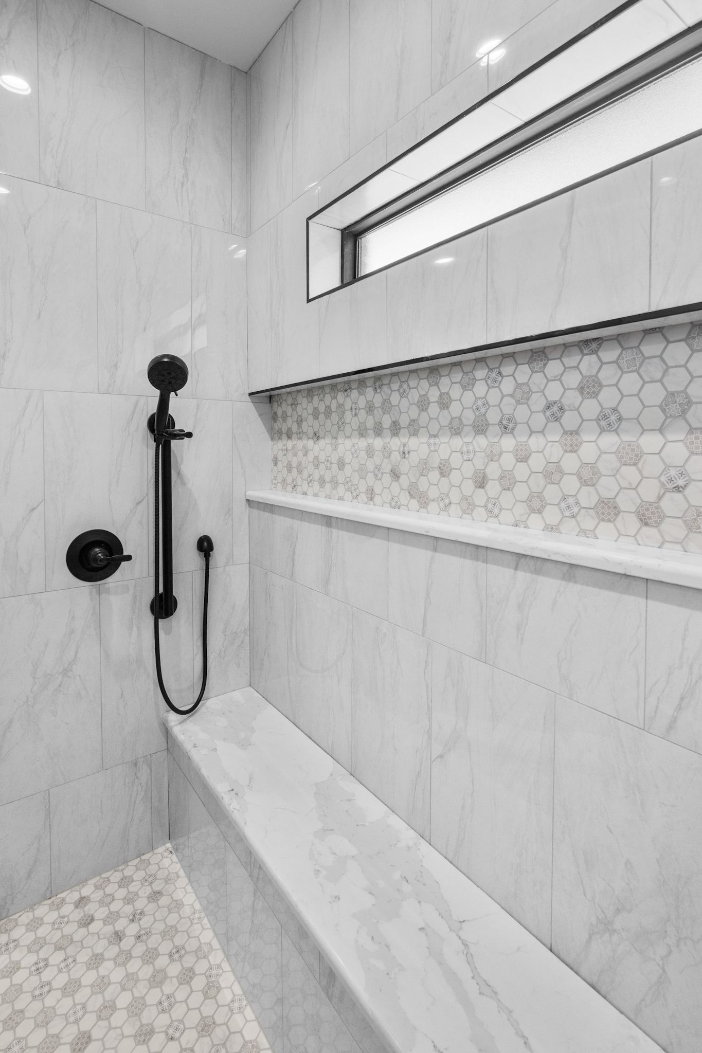 Shower with white marble-look tile, black fixtures, built-in bench, and honeycomb tile accent.