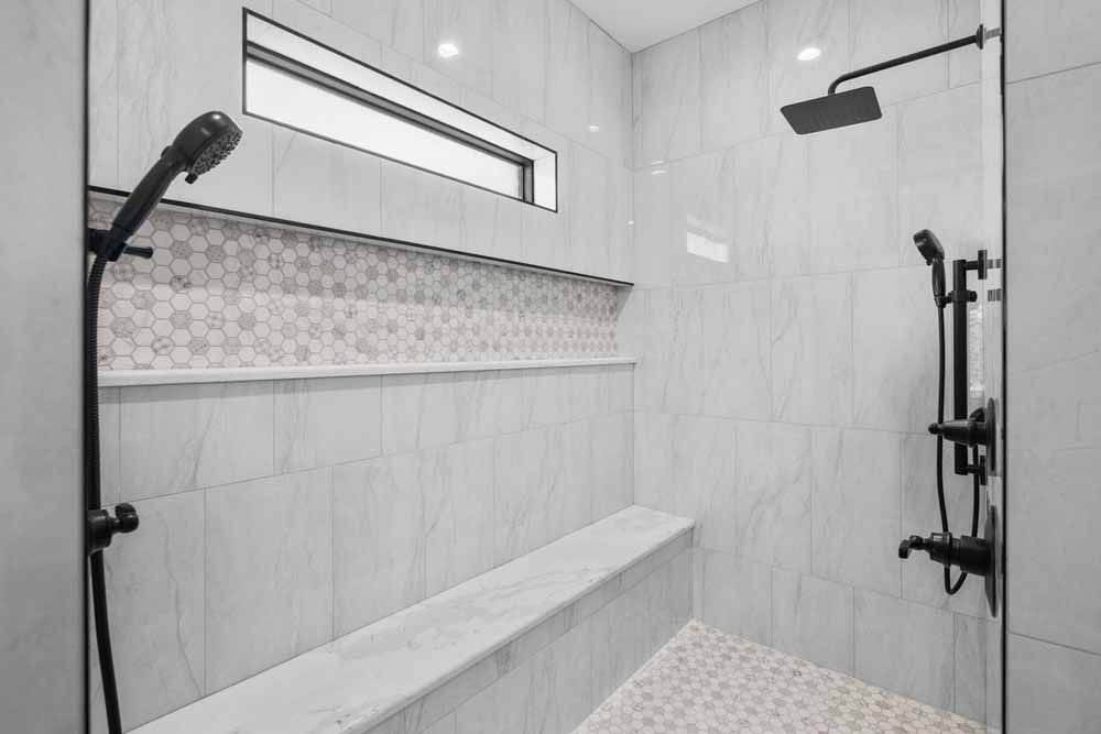 Modern shower with gray tile, bench, and black fixtures. Built-in shelf with decorative mosaic tile.