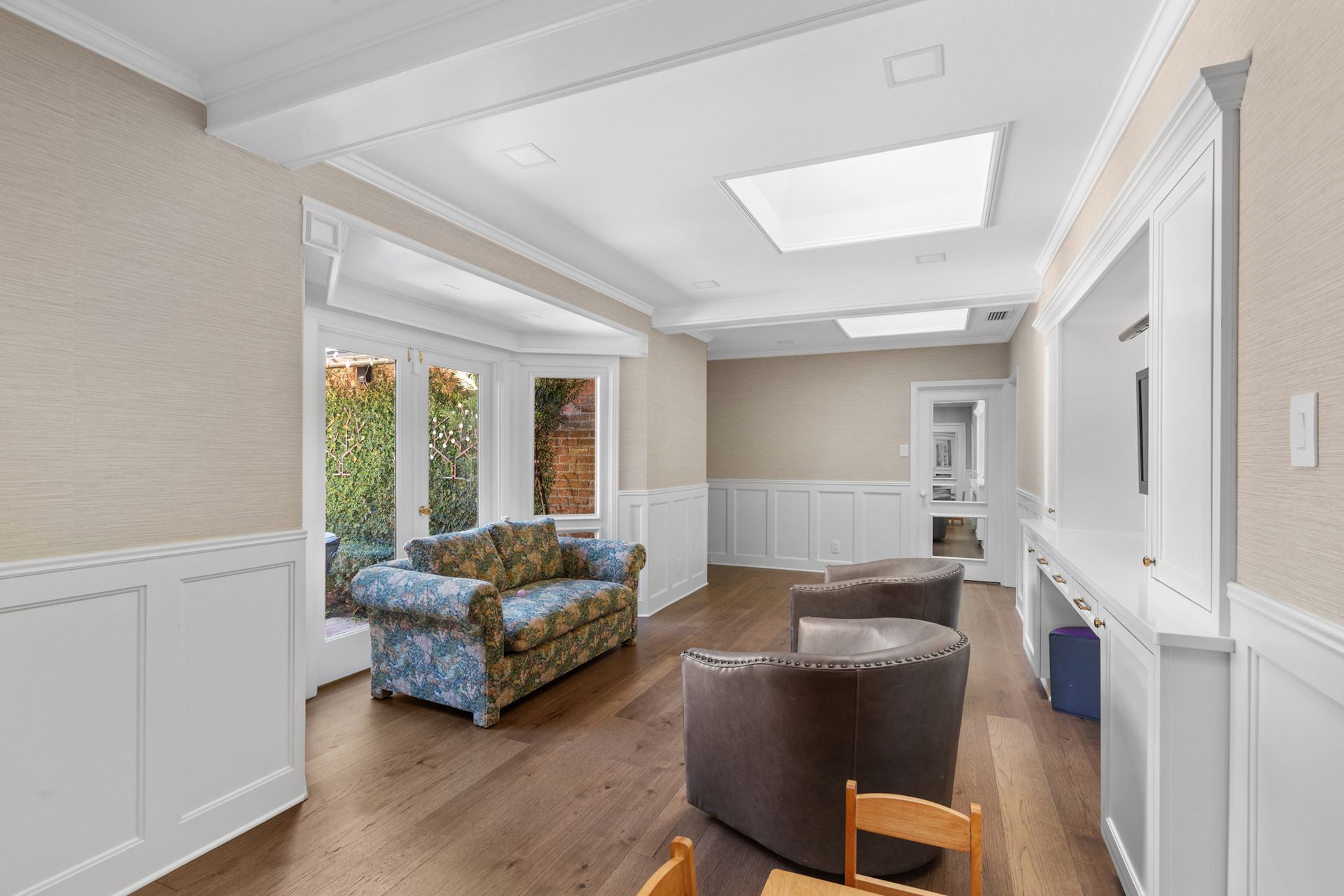 Sunroom with wood floors, cream walls, and white wainscoting. Includes a patterned couch and two brown chairs.