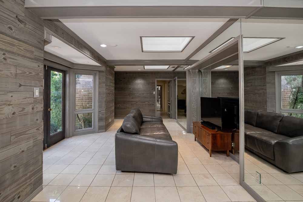 Living room with gray paneled walls, gray leather sofas, TV on a wooden console, and mirrored wall.