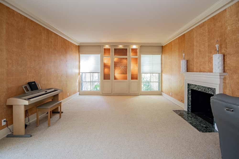 Empty living room with patterned orange walls, piano, fireplace, and windows with white shades.