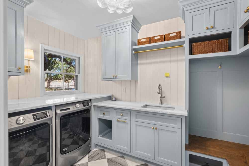 Laundry room with blue cabinets, white countertops, and washer/dryer. Checkered floor and window.
