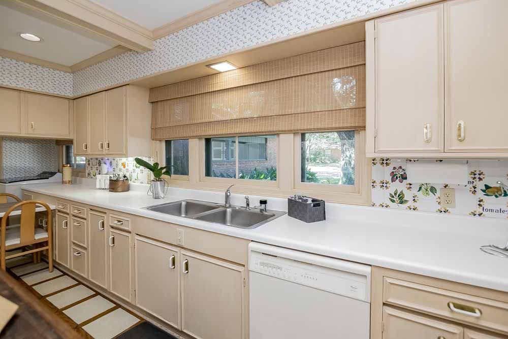 Kitchen with beige cabinets, white countertops, stainless steel sink, and window with bamboo shade.