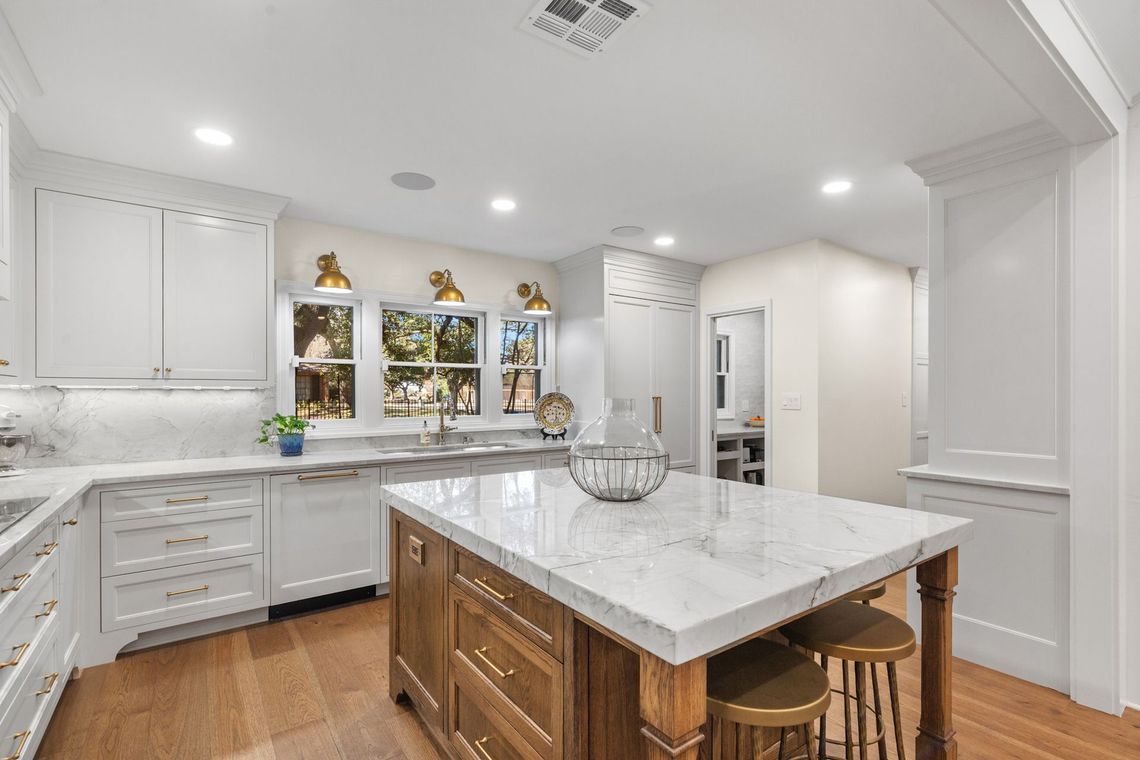 White kitchen with island, marble countertops, wooden cabinets, and stools.