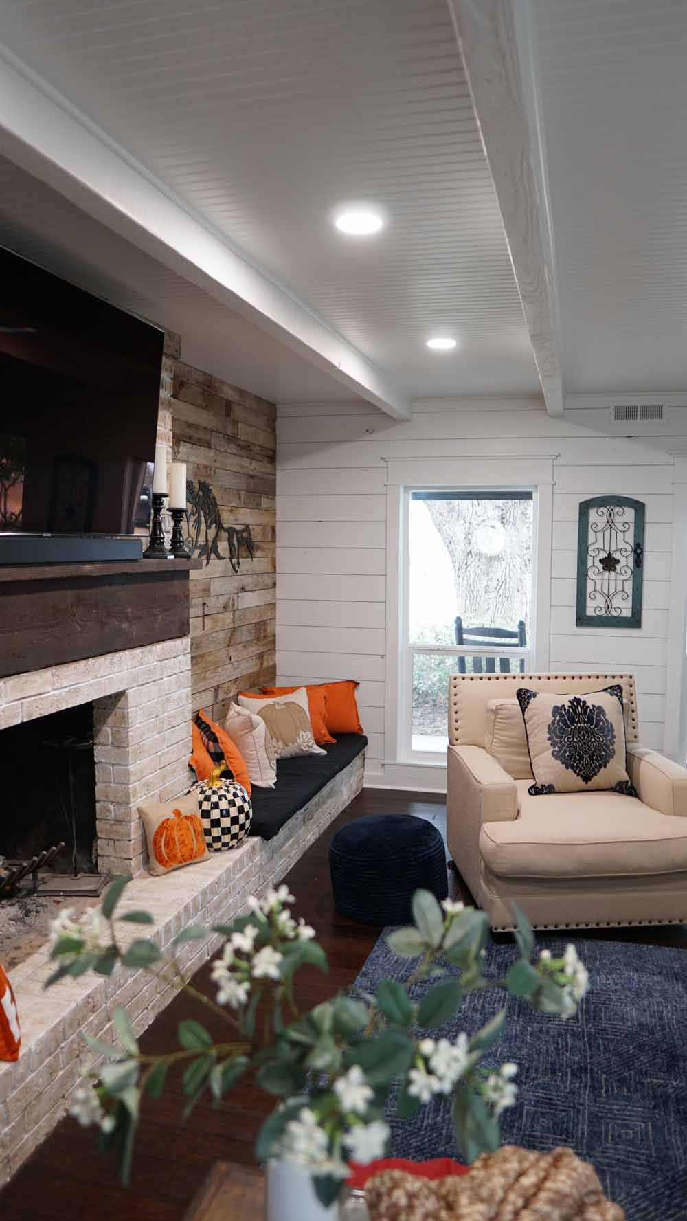 Cozy living room with fireplace, built-in bench, and cream-colored armchair. Orange and black pillows add pops of color.