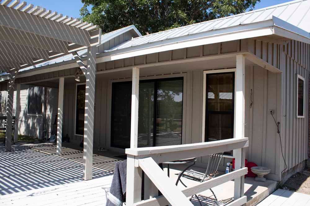 A beige-painted house with a porch and pergola, casting shadows.