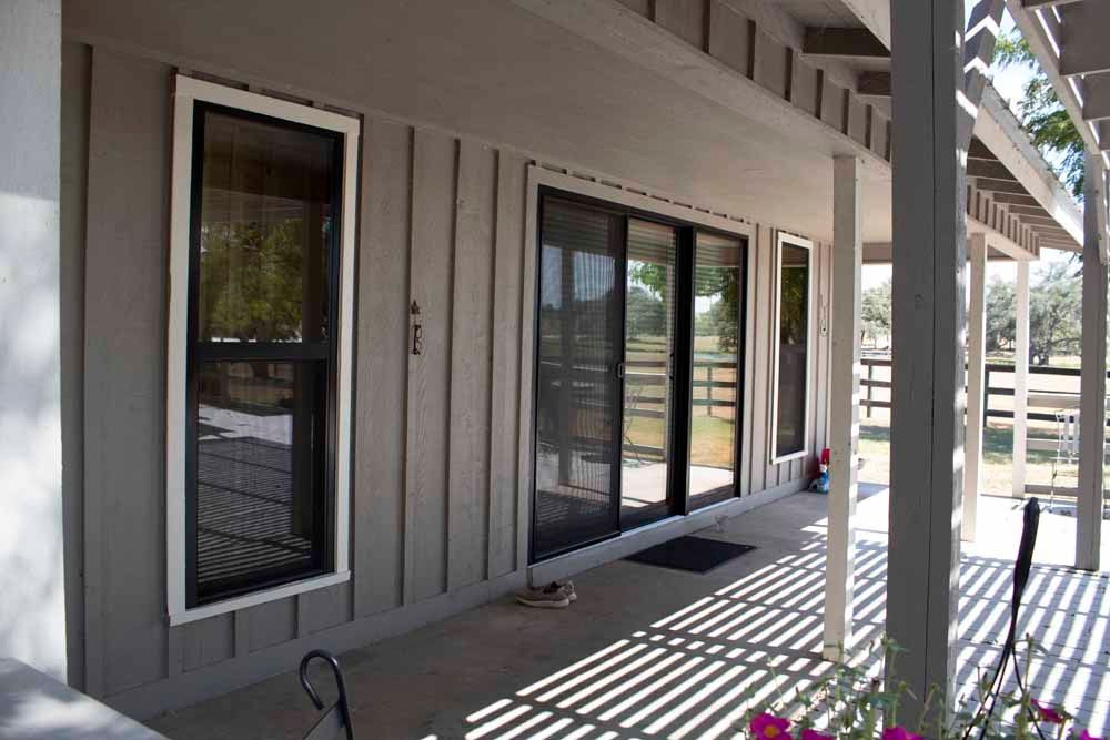 Grey house exterior with sliding glass doors, covered porch, and a view of a fence.