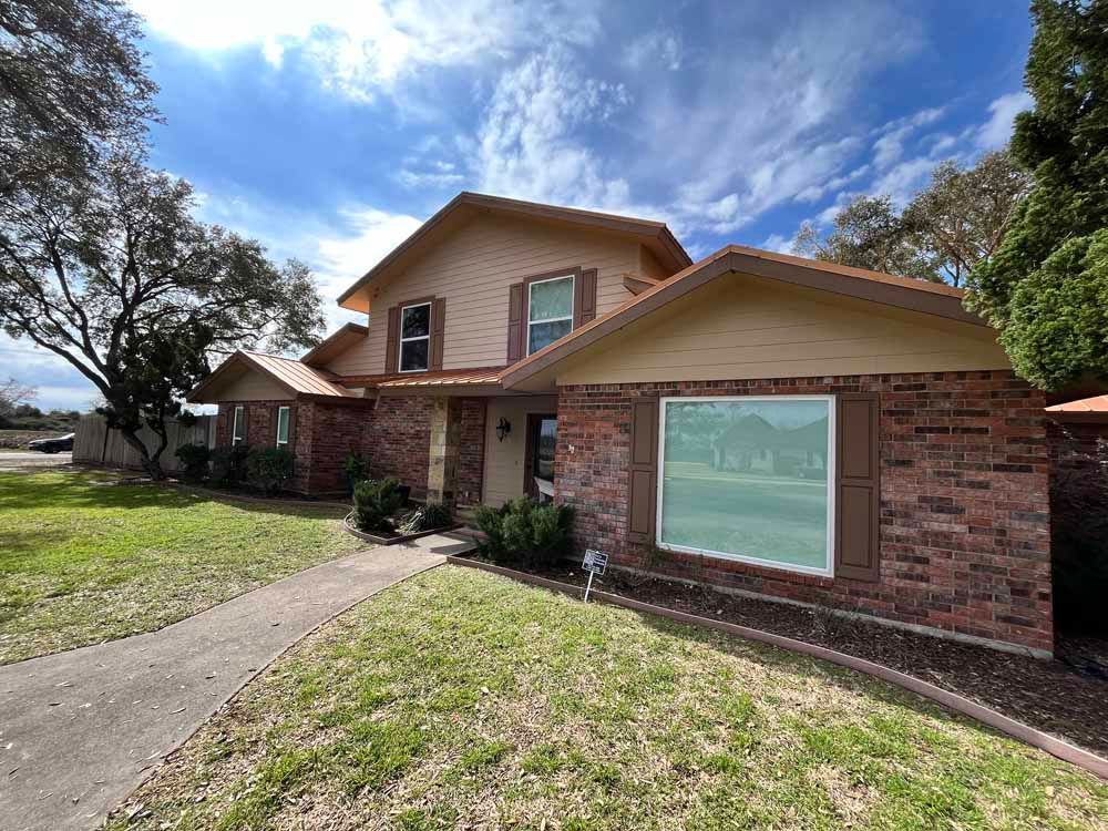 Two-story brick house with brown shutters and trim, set on a green lawn under a partly cloudy sky.