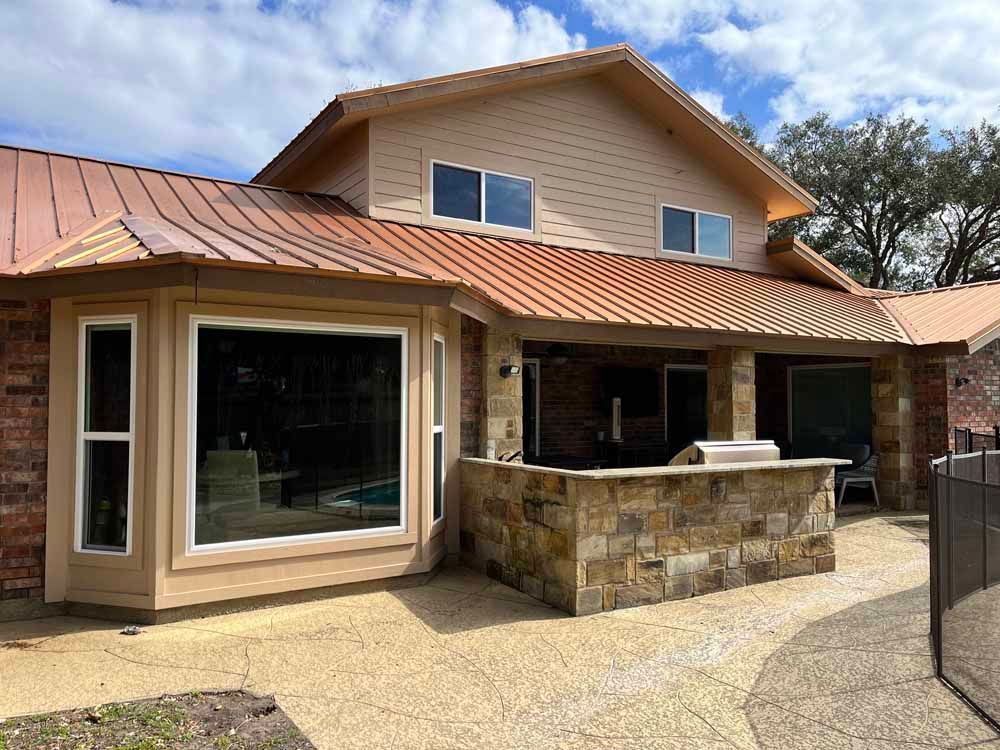 A house with copper roof and brick facade, a bay window, and a stone outdoor kitchen.