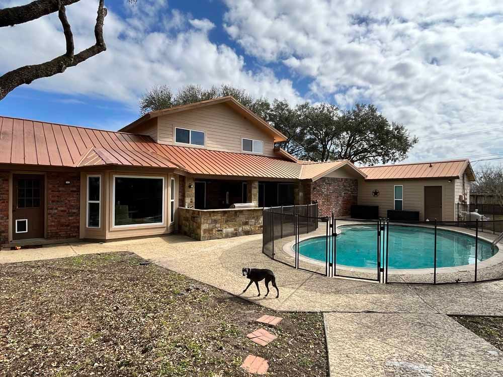 House with copper roof, pool, and dog in yard on a cloudy day.