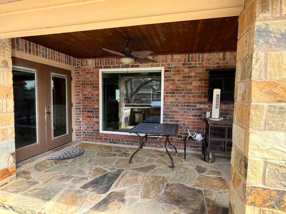 Covered patio with brick wall, stone floor, double doors, window, and fan.