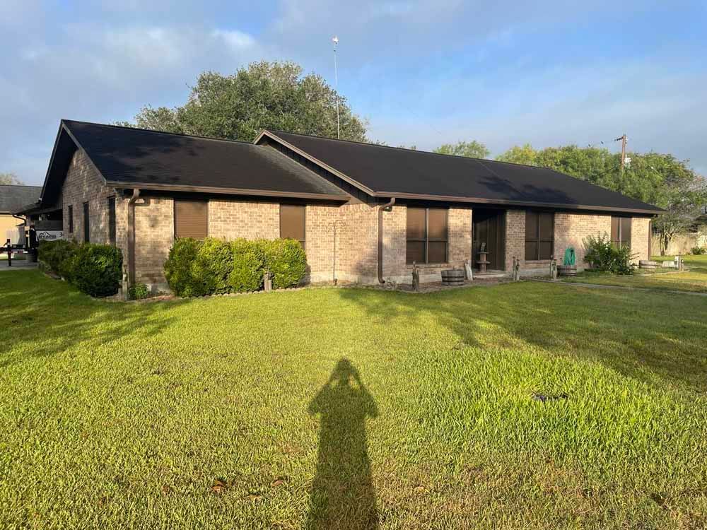 Brick house with black roof, brown shutters, and green lawn; a shadow of the photographer is cast on the grass.